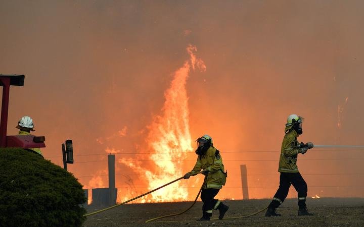 This picture taken on December 31, 2019 shows firefighters working to stop a fire reach a house as bushfires hit the area around the town of Nowra in the Australian state of New South Wales. - 