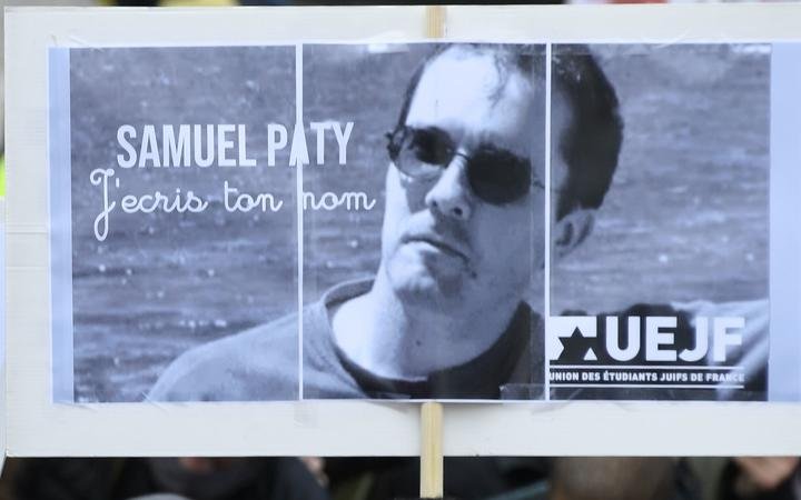 A person holds a placard with the portrait of history teacher Samuel Paty as people gather on Place de la Republique in Paris on October 18, 2020, two days after he was beheaded by an attacker who was shot dead by policemen. 