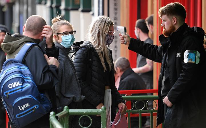 A security guard uses a handheld thermometer to take the temperature of customers, as they wait to enter a bar in Liverpool, north west England on October 2, 2020, following the announcement of new local restrictions in the northwest 