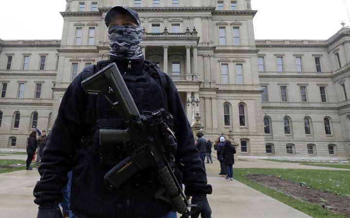 (FILES) In this file photo taken on April 15, 2020, an armed protester stands outside the Michigan State Capitol in Lansing, Michigan, during a demonstration against Michigan Governor Gretchen Whitmer's expanded the states stay-at-home order to contain the spread of the coronavirus. - 