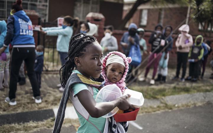 A child holds a sibling while carrying a food parcel received from the grassroots charity Hunger has no Religion in Johannesburg, on May 25, 2020 (Photo by MARCO LONGARI / AFP)