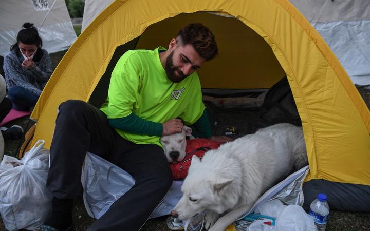 A man pets one of his dogs as he is sheltered in a tent in Izmir, on November 1, 2020 after a powerful earthquake struck Turkey's western coast and parts of Greece. - 