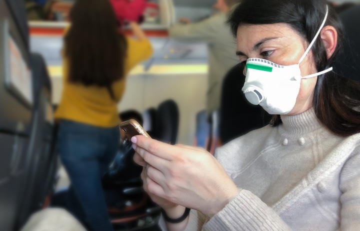 Airplane passenger with with respiratory mask looking at phone.