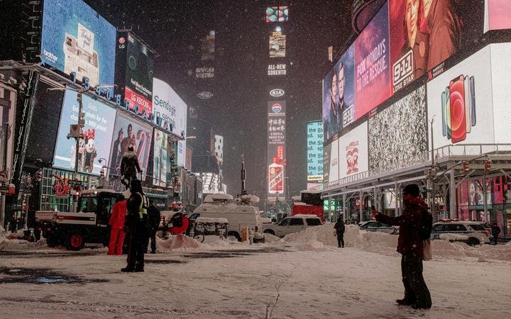 A man takes a photo as snow continues to fall in Times Square, NYC.